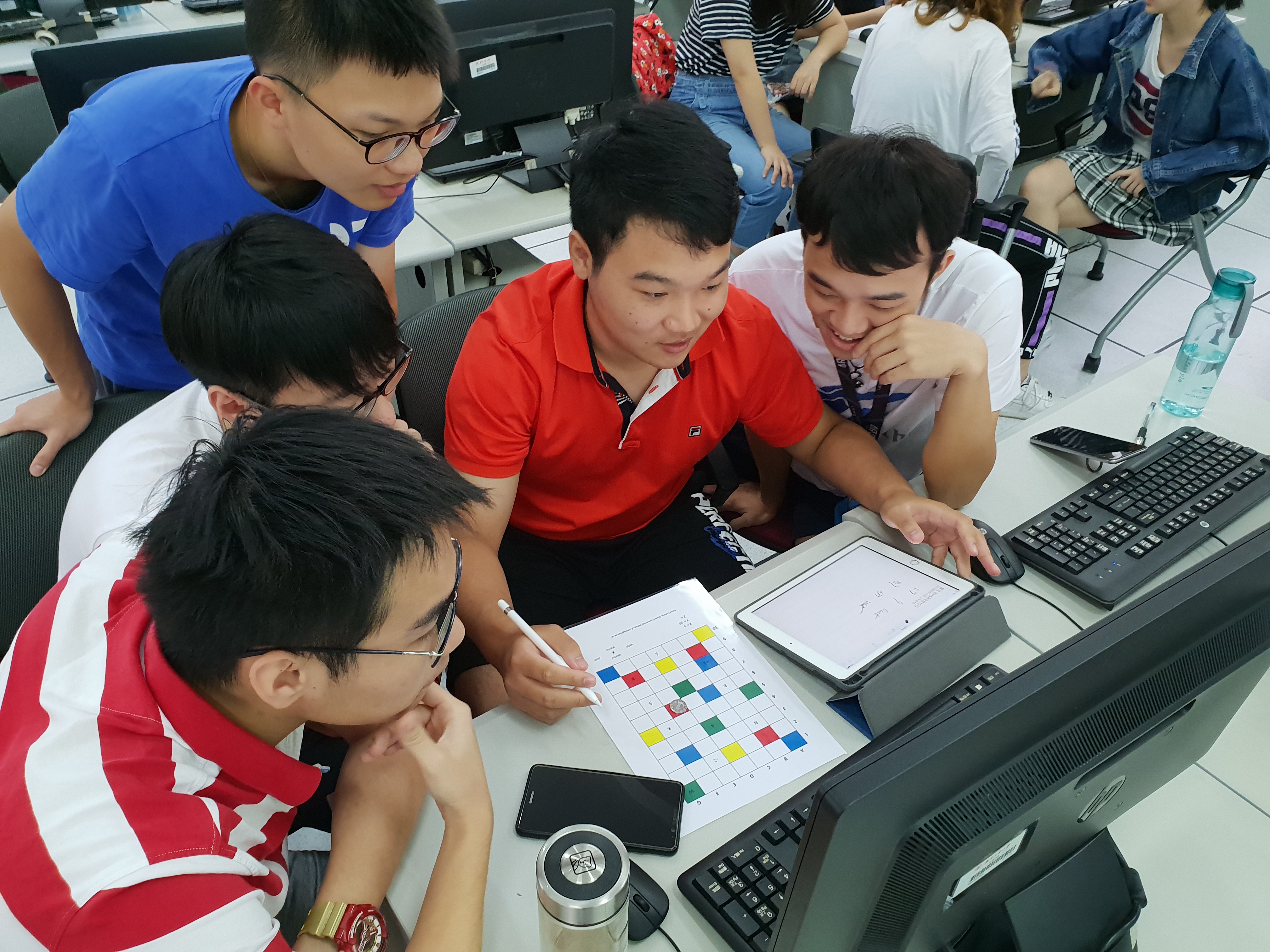 Five students work together on a ProgBoard printed on a sheet of paper.