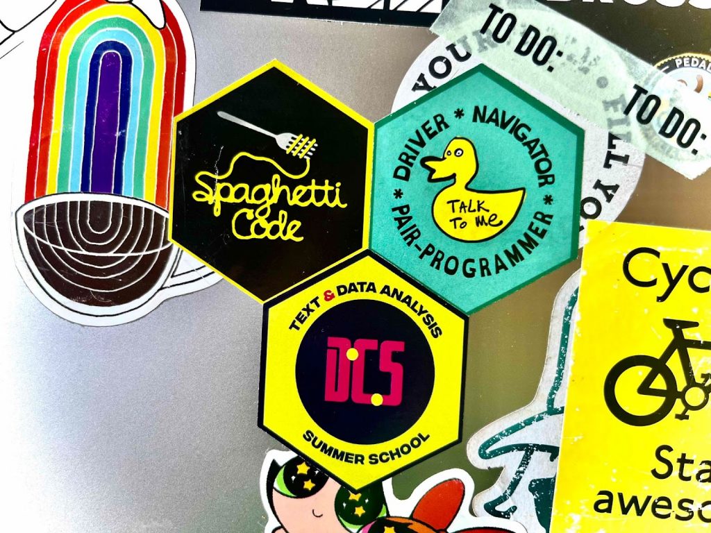 photo of stickers on a laptop. One sticker says 'Text and Data Analysis DCS Summer School'.
